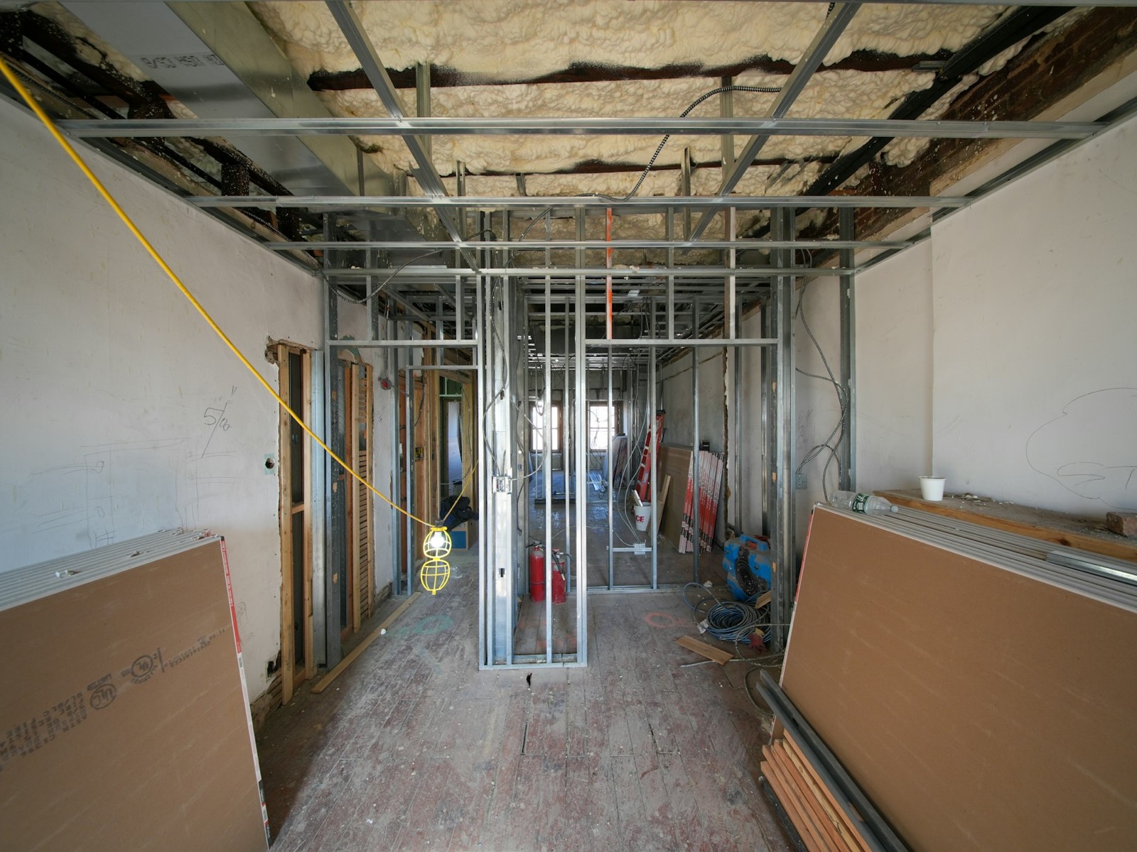 An office floor mid fit-out: metal stud partitions framed, plasterboard stacked against the walls, daylight from the far windows